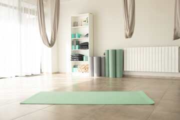 Gym interior with green yoga mat, big windows, no people. Copy space. - obrazy, fototapety, plakaty