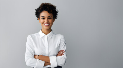 A stylish black woman with curly hair and a bright smile, donning a crisp white shirt and sleek black pants, stands against an indoor wall, her shoulder and neck adorned with intricate sleeve
