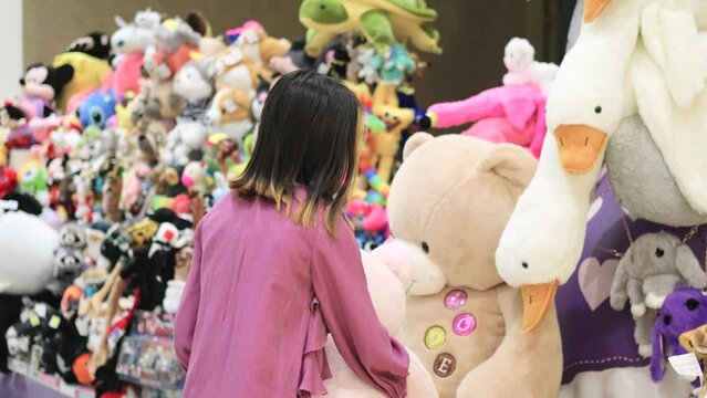 A little girl in a lilac elegant dress against the background of soft toys in a store. A child chooses a toy as a gift