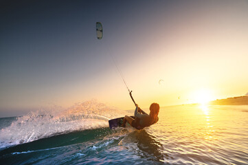 girl kiter rides against a beautiful background of splashes and a colorful sunset of the sea. Woman...