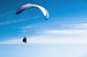 paraglider flies in the blue sky against a background of clouds and blue sky. Paragliding in the sky on a sunny day