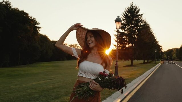 Beautiful hipster woman holding bunch of wildflower walking at sunset
