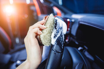 Young woman cleaning the steering wheel of car using a special brush with foam
