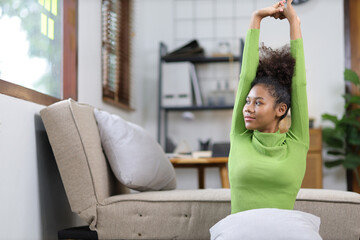 Attractive african american woman stretching to relax in living room at home.
