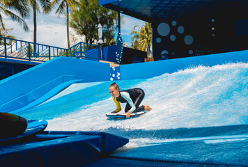 Beautiful young woman surfing on a wave simulator at a water amusement park