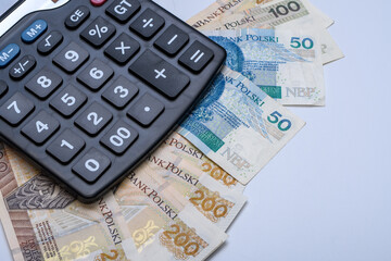 Pieniądze, polskie banknoty PLN leżą na biurku obok kalkulatora - obrazy, fototapety, plakaty