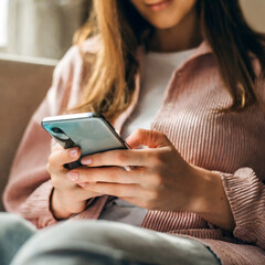 Close-up of beautiful young Caucasian woman using cell phone in living room, Asian woman holding and looking at smartphone screen in the living room