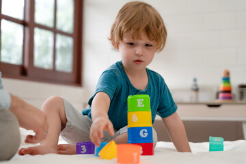 Happy kid building a tower from plastic colorful blocks, child physical muscle development and creativity at home with family. Kindergarten learning toys evolution playing.
