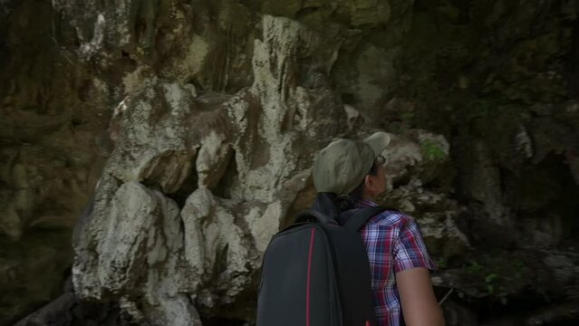Geologist woman in casual dress with digital tablet exploring a cave formed by limestone mountain in the park. Turn around and pull back moves shot. 