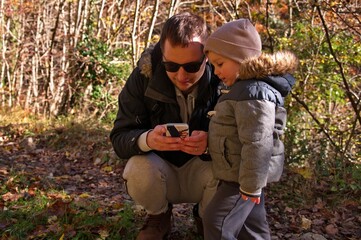 Father and his toddler using mobile phone in the forest