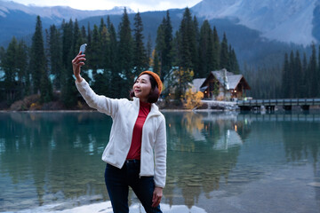 Senior woman travelers visit the Emerald Lake in Alberta, Canada during winter. Happiness tourists making selfie by using smartphone to capture photo. Tourism, adventure, wild road, road trip