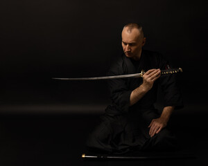 Portrait of aikido sensei master with black sensei belt in taekwondo kimono witn sword katana on...