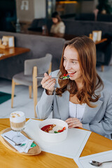 Young attractive woman enjoys tasty meal on cafe or restaurant background