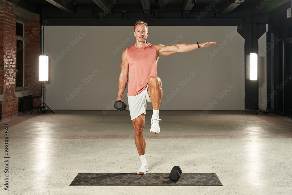 Wall mural a young caucasian athlete stands on one leg, moves his arm to the side and raises his leg, and holds