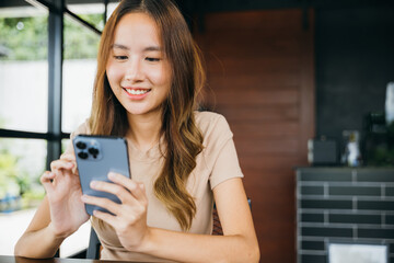 Beautiful Asian female has transfer money financial internet banking on mobile phone, young woman using smart phone for shopping online at cafe coffee shop near windows in the morning