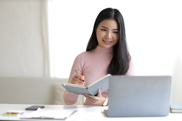 Fototapeta na wymiar Young Asian woman working with laptop and financial income and expenses record document at home.