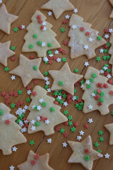 Christmas cookies in shape of star and tree on wooden table with green, red and white star shaped sprinkles. Christmas festive background on selective focus