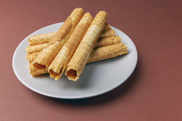 Fototapeta na wymiar Fresh buttered waffle tubes on a plate on a brown background