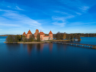 Low down drone picture of Trakai castle surrounded by lake Galve (Galvė) with a bridge leading up to it located in Trakai, Lithuania