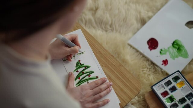 A left-handed woman signs a homemade New Year's card with a green felt-tip pen. Over the Shoulder Shot plan