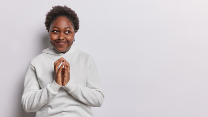 Horizontal shot of dark skinned plump African woman steeples finger schemes something looks aside...