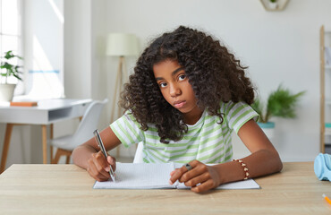 Portrait of a school child while doing homework. Beautiful African American girl sitting at her...