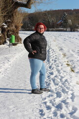 Fototapeta na wymiar A young red-haired woman in a black jacket and blue jeans lies on the snow in winter