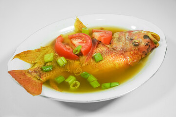Tilapia fish soup in a bowl with turmeric sauce and spices, using sliced tomatoes and spring onions as garnish - Isolated on white backgrounds. Concept for whole healthy food, omega-3, animal protein.