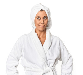 Middle-aged woman with towel post-shower in studio confused, feels doubtful and unsure.