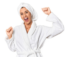 Middle-aged woman with towel post-shower in studio raising fist after a victory, winner concept.