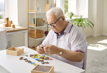 Elderly man is putting together a puzzle in a modern dementia rehabilitation center. Creative idea of memory loss training during dementia, Alzheimer's disease. The concept of human mental health. - obrazy, fototapety, plakaty