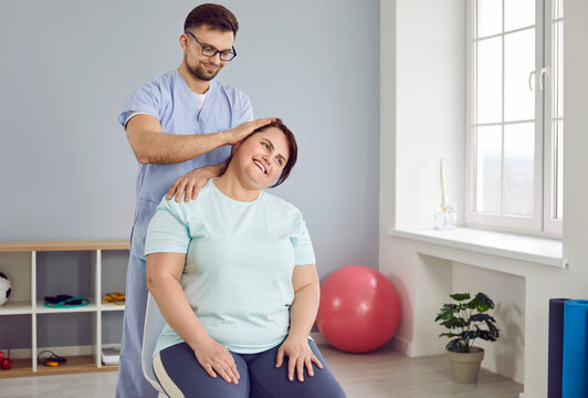 Male doctor, chiropractor, osteopath, physiotherapist or manual therapist at medical rehabilitation center doing manipulations over neck of happy plus size woman patient