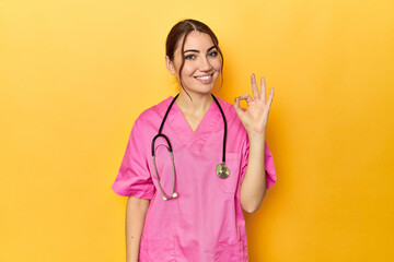 Nursing assistant in yellow background cheerful and confident showing ok gesture.