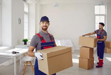 Portrait of smiling young man mover worker in uniform holding a cardboard box and looking cheerful...