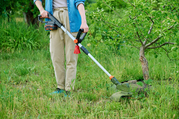Woman mowing grass with cordless trimmer in garden