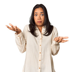 Young Filipina with long black hair in studio doubting and shrugging shoulders in questioning...