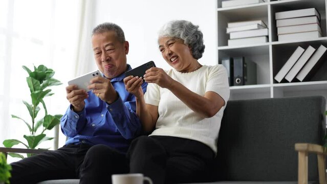 Happy senior couple in retirement at home. Senior couple sitting on the sofa playing mobile phones in the living room at home.