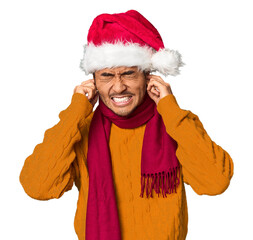 Young Chinese man with red hat, scarf in studio covering ears with hands.