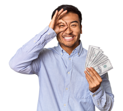 Young Chinese man holding dollar bills in studio excited keeping ok gesture on eye.