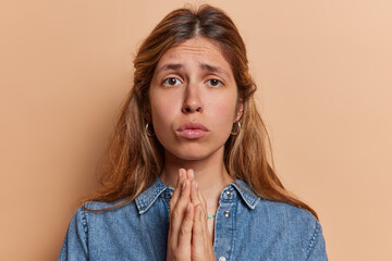 Photo of displeased young European woman begging for something holding hands folded in prayer pose...