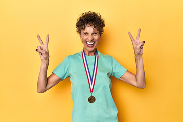 Proud sportswoman displaying her winning medal on yellow studio background