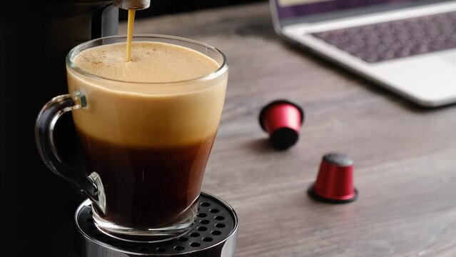 Close-up of coffee being poured into a glass cup in a capsule coffee machine.