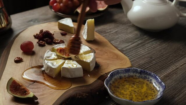 A man pours honey over a dessert made from Camembert cheese and fruit. Cooking a romantic dinner at home.