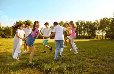Naklejka na ściany i meble Group of a kids friends playing outside in the park standing in a circle and holding hands. Happy children playing games and having fun outdoor on a sunny summer day in casual clothes.