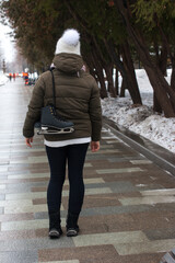 A woman walks in a winter park with skates on her shoulder. Coming from training