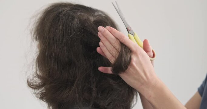 Cut off lock of hair. Woman's hand cuts off lock of hair on man's head with scissors. Back view, unrecognizable. Stiff long hair.