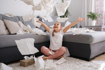 The process of creating a mess by a child. Little girl scatters napkins in living room