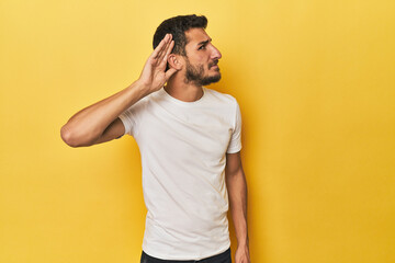 Fototapeta na wymiar Young Hispanic man on yellow background trying to listening a gossip.