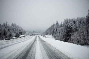 Photo of the winter road during the snowfall in Magadan, Russia. Snow showers on the trees and...