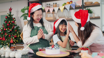 Happy Grandmother, mother and little daughter decorated cake together for Christmas Eve. Three generations Asian women making cake for Christmas day. Christmas cake decorated. Festive holiday